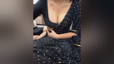 Media: Video of a woman in a black polka-dotted sari, her cleavage visible as she adjusts her neckline, revealing medium-sized breasts.