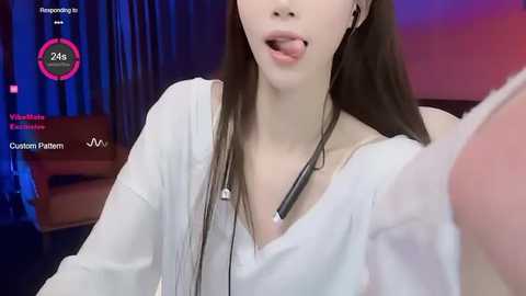 Media: Video of an Asian woman with long black hair, wearing a white shirt and microphone headset, with blurred background featuring a pink couch.