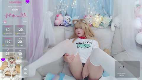 Media: A video of a young woman with light skin and blonde hair, dressed in a white shirt and thigh-high stockings, reclining provocatively on a bed. The background features pastel decor with stuffed animals.