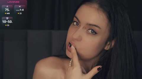 Media: Video of a young woman with long black hair, light skin, and dark eyes, biting her finger, with a dark background. Her nails are painted black.