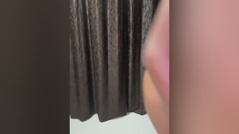 Media: Video of a person's hand holding a black velvet curtain. The hand, with light skin tone, is blurry, while the curtain's texture is clear. The background is a white tiled floor.