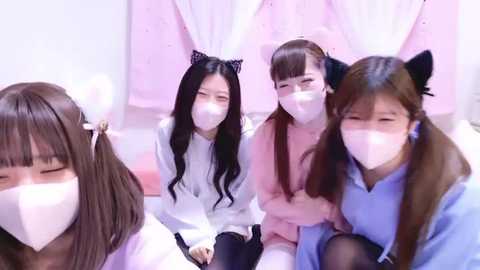 Media: Video of four Asian women in white masks, wearing white shirts, black cat ears, and pink headbands, seated in a soft pink room, smiling.