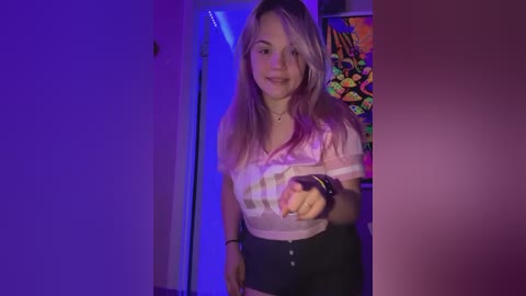 Media: Video of a young Caucasian woman with long, light brown hair, smiling, wearing a pink plaid shirt and black high-waisted shorts. She stands in a dimly lit room with purple and blue lighting, a colorful wall poster behind her.