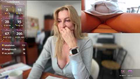 Media: A video shows a blonde woman in a low-cut gray top, biting her finger, with a close-up of her exposed breast. The background is a messy office.