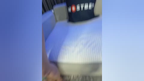 Media: A blurry video of a person sitting on a beige couch with a black cushion, wearing a dark cap with white text.