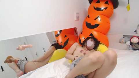 Media: A video of an Asian woman lying on a bed, wearing a grey shirt, with her breasts exposed, sleeping on her back. The room features a large orange pumpkin with a smiling face and a yellow beanbag.