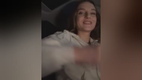 Media: Video of a young woman with straight, light brown hair, smiling, wearing a beige hoodie, in a dimly lit car. The background is blurred, with a black and white gradient.