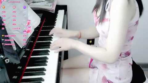 Media: Video of an Asian woman with long hair, wearing a pink sleeveless dress, playing a black piano. The background is a minimalist white room.