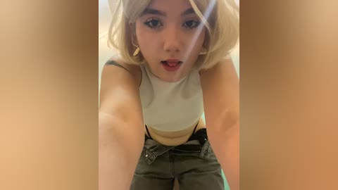 Media: A video of a young Asian woman with shoulder-length blonde hair, wearing a white tank top and denim shorts, leaning forward with a surprised expression.