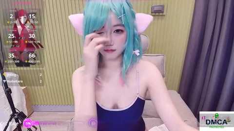 Media: Video of a young woman with teal hair, wearing a black tank top and cat ears, seated at a desk. Background shows a green wall, a computer screen with game statistics, and a DMC logo.