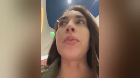 Media: Video of a woman with fair skin, dark hair, and neutral expression, taken from a low angle, showing her from the shoulders up.