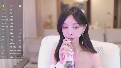 Media: Video of an Asian woman with long black hair, wearing a white dress, drinking water, in a modern, brightly lit room.