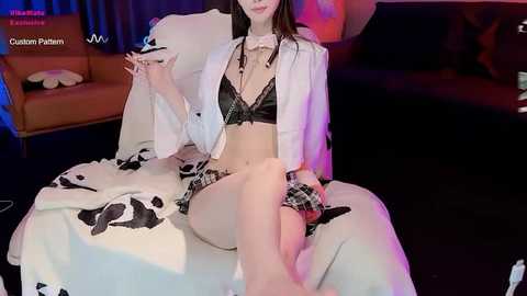 Media: Video of a slender, fair-skinned Asian woman in black lingerie and white robe, sitting on a plush couch in a dimly lit room with blue and pink lighting.