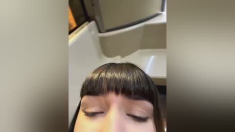 Media: Video of a person with straight, dark brown hair and blunt bangs, eyes closed, sitting in an airplane. The image is taken from a low angle, focusing on the person's face and upper body.