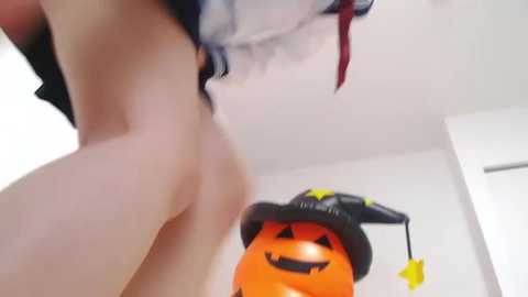 Media: Video of a pale-skinned person wearing a black witch hat and red-striped stockings, standing near an orange pumpkin with a star decoration.