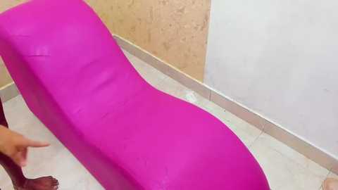 Media: Video of a vibrant, bright pink, wavy-shaped lounge chair placed against a beige, textured wall and a white, tiled floor.