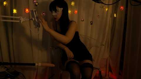 Media: Video of a slender, fair-skinned Asian woman in black lingerie, white mask, and stockings, adjusting IV bag in dimly lit hospital room with string lights and medical equipment.