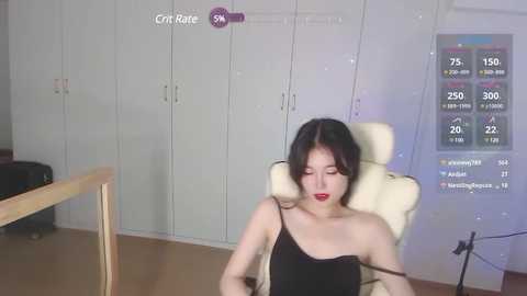 Media: Video of an Asian woman with long black hair, wearing a black strapless dress, sitting in a white recliner chair. A digital fitness tracker screen displays workout stats in the background.