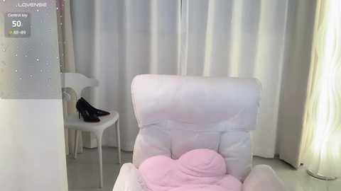 Media: Video of a minimalist, modern room with white walls, floor, and curtains. A white armchair with a pink cushion is centrally positioned. A black shoe rests on a white stool to the left. A white lamp with a curved shade stands to the right.