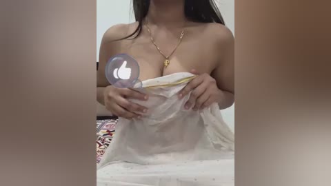 Media: A video of a woman with long black hair, holding a white sheet over her breasts, wearing a gold necklace. Her face is partially obscured by a Facebook logo.