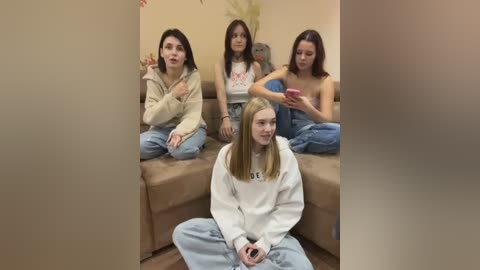 Media: Video of four young women in casual attire, sitting on a beige sofa, engaged in conversation, with a fifth woman seated on the floor in front.