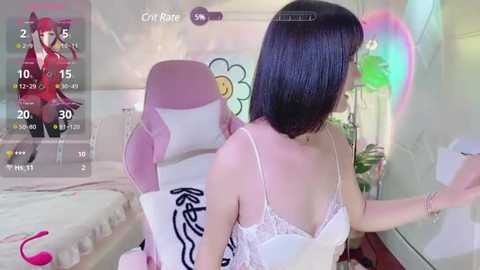 Media: Video of an Asian woman with straight black hair, wearing a white lace bra, sitting on a pink gaming chair in a colorful, anime-themed bedroom.