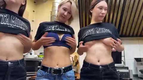 Media: Video of three topless women in a kitchen, lifting their black \"T&A Minnesota\" t-shirts to reveal blue bras and bare breasts.