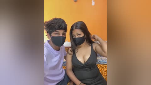 Media: Video of a young couple wearing black face masks, the woman in a black dress, the man in a white shirt, seated on a leopard-print couch in an orange-walled room.