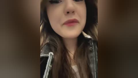 Media: Video of a young woman with long brown hair, wearing a black leather jacket, and a neutral expression.