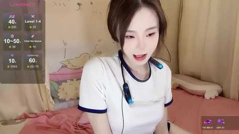 Media: A video of an Asian woman with fair skin, brown hair, and small breasts, wearing a white T-shirt, sitting on a bed with pink sheets, smiling.