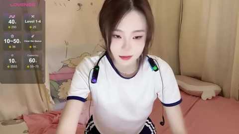 Media: Video of a young Asian woman with light skin, brown hair, and red lipstick, wearing a white T-shirt, seated on a bed with pink sheets, with a virtual reality headset on.