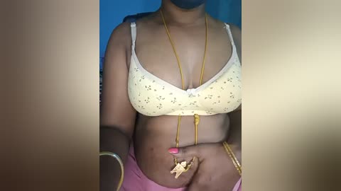 Media: Video of a dark-skinned woman wearing a yellow bra with small polka dots, gold necklace, and pink skirt.