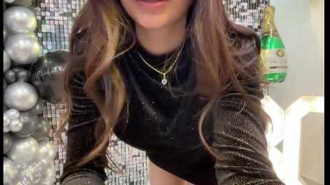 Media: Video of a woman with long, wavy brown hair, wearing a black glittery crop top, silver necklace, and black gloves. Background features shiny metallic tiles and a green champagne bottle.