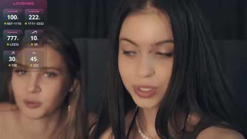 Media: Video of two young women with long black hair, one wearing a black top, the other partially visible, in a dimly lit room.