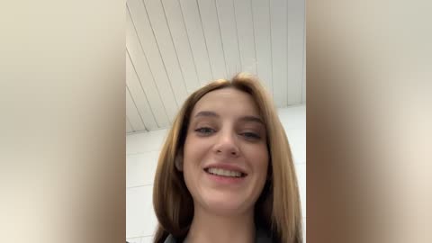 Media: A video of a young woman with long, straight, light brown hair, fair skin, and a friendly smile, standing in a room with white walls and a sloped ceiling.