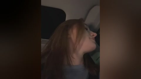 Media: A dimly lit video captures a young woman with shoulder-length, straight brown hair, wearing a light-colored shirt. She is looking upwards, possibly in a car, with the car's interior visible in the background.