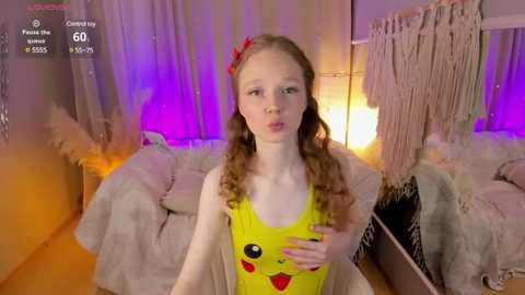 Media: Video of a young girl with long, curly brown hair and a red bow, wearing a Pikachu onesie, standing in a cozy, dimly-lit room with hanging macram\u00e9 and a bed.