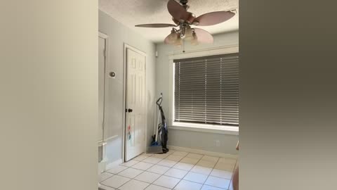 Media: Video of a minimalist, well-lit bedroom with beige walls, white door, closed blinds, and a ceiling fan.