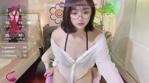 Media: Video of an East Asian woman with straight black hair, wearing a white off-shoulder top, sitting on a chair in a room with a floral background.