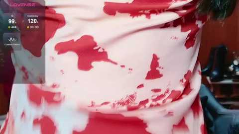 Media: Video of a person wearing a red and white spotted dress, showcasing a close-up of their stomach and chest area. The background is a blurred indoor setting with a chair.