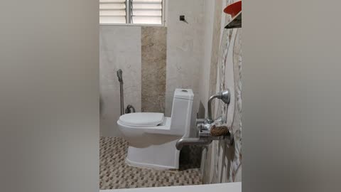 Media: A video of a modern, compact bathroom with a white ceramic toilet, beige mosaic tiles, and a small window with horizontal blinds. The floor is covered with small, textured beige tiles.