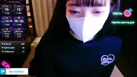 Media: Video of a young Asian woman in a black shirt, wearing a white surgical mask, with a virtual reality headset displaying a live stream of her face, in a dimly lit room.