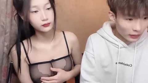 Media: Video of an East Asian woman in black sheer lingerie and a man in a white hoodie, both looking serious.