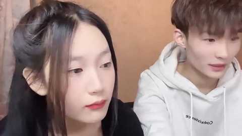 Media: Video of a young East Asian woman with long black hair, wearing red lipstick, and a young East Asian man with short brown hair, both looking contemplative.