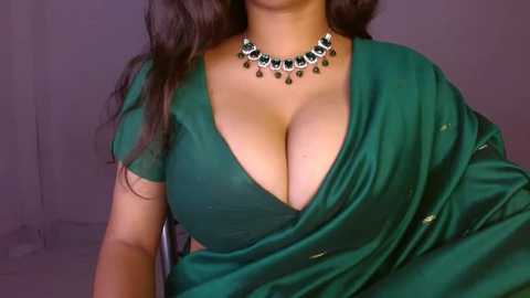 Media: Video of a South Asian woman with medium brown skin, wearing a deep green sari with a plunging neckline, revealing ample cleavage. She sports a decorative necklace with a matching green stone.