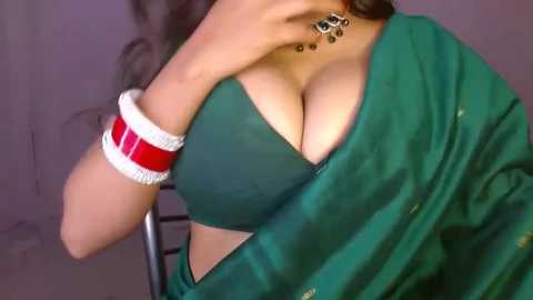 Media: Video of a woman with light skin wearing a green blouse that reveals cleavage, a red wristband, and a green sari draped over her shoulders.