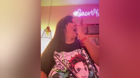 Media: Video of a plus-sized woman with black hair and glasses, wearing a black T-shirt with a colorful anime character, in a dimly lit room with a neon sign and a hanging lamp.