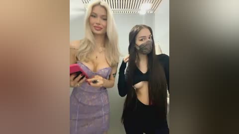 Media: Video of two young women in a modern elevator. One is blonde, wearing a strapless purple dress, holding a pink phone. The other is brunette, masked, wearing a black crop top.