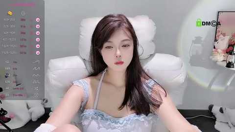 Media: A video of an Asian woman with straight black hair, wearing a blue lace bralette, sitting on a white chair in a dimly lit room with a green screen.