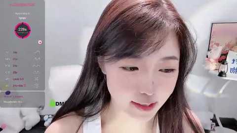 Media: Video of a young East Asian woman with long dark hair, fair skin, and red lipstick, wearing a white top, in a modern bedroom with a white bed and wall.